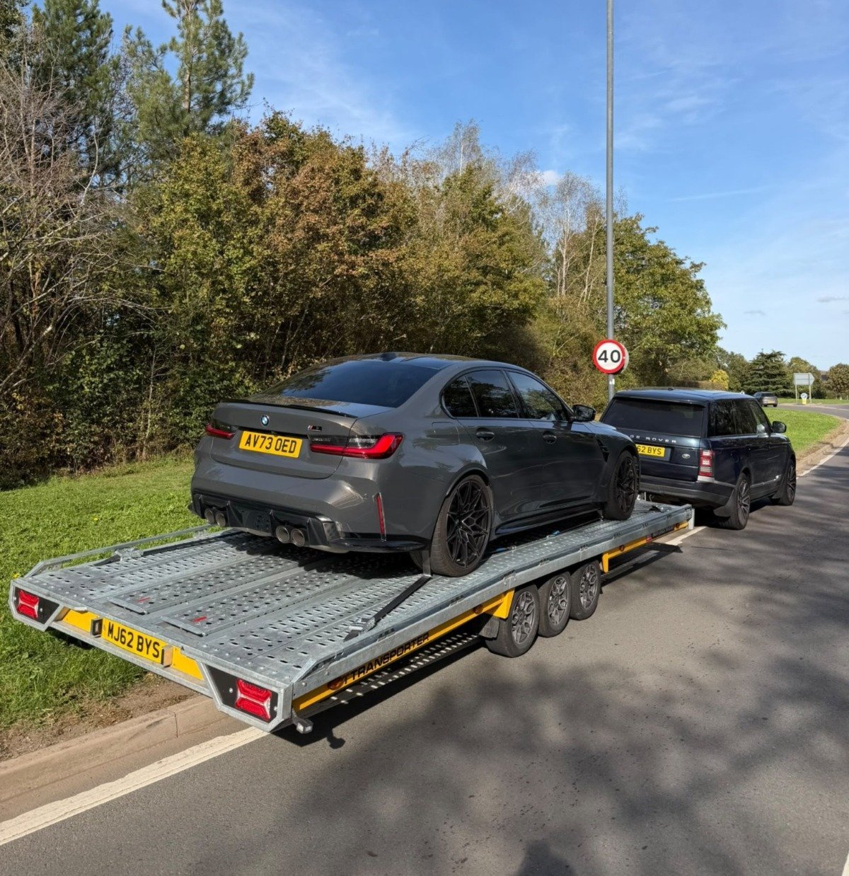 Dark gray sedan loaded on a flatbed tow truck in a parking lot with trees and green grass in background